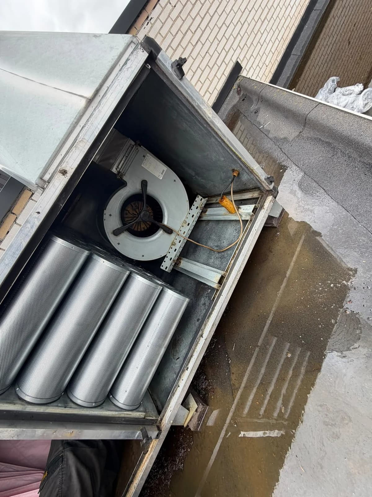 Top-down view into an open rooftop odor unit showing carbon cylinders and centrifugal fan.
